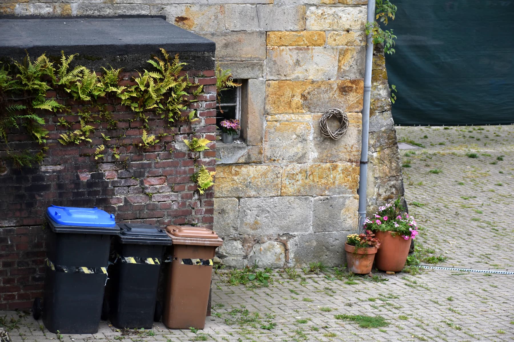 Drei Mülltonnen an einer Steinmauer im gepflasterten Innenhof